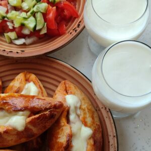 Close-up of Turkish pide with melted cheese, fresh salad, and two glasses of Ayran on a table.