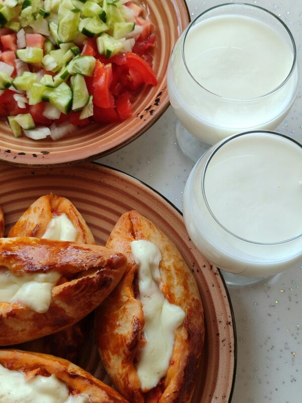 Close-up of Turkish pide with melted cheese, fresh salad, and two glasses of Ayran on a table.