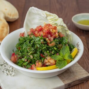 Vibrant tabbouleh salad with fresh ingredients, served with pita bread and lemon wedges.