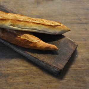 Close-up of a delicious golden-brown baguette placed on a rustic wooden board, highlighting its artisanal texture.