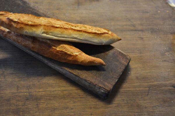 Close-up of a delicious golden-brown baguette placed on a rustic wooden board, highlighting its artisanal texture.